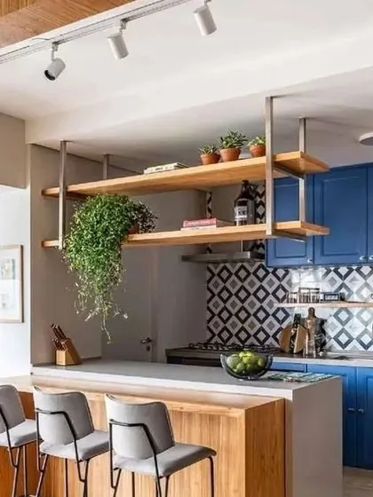 A trendy kitchen design featuring a breakfast bar with hanging wooden shelves. The bold blue cabinets and patterned backsplash create a vibrant and social atmosphere, making the kitchen more than just a place to cook.