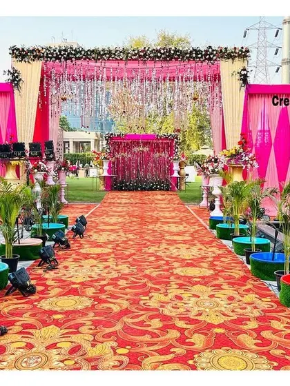 A full view of a vibrant outdoor entrance. The bright pink walls, patterned carpet, and small water fountains create a festive and welcoming atmosphere for a daytime event.
