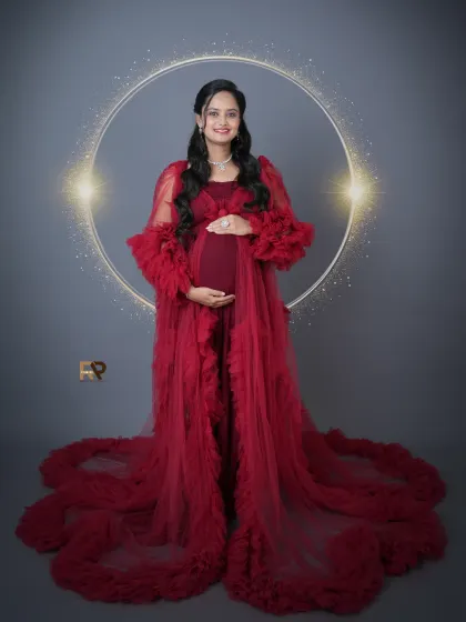 A circle of light. This solo portrait uses a glowing ring prop to create a halo effect, beautifully framing the mom-to-be in her flowing red gown.