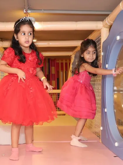 Two girls in beautiful party dresses exploring the different levels of the indoor play gym.