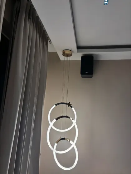 A wall mounted surround speaker placed carefully to blend with the room's aesthetics, right next to a modern chandelier. My goal is always to integrate the technology into your home's design as seamlessly as possible.