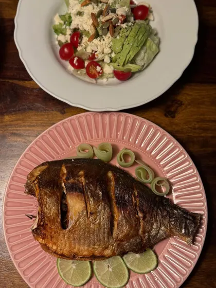 Our roasted whole fish served on a pink plate with a side salad. This dish showcases our simple and honest approach to cooking, focusing on fresh ingredients and bold flavors.