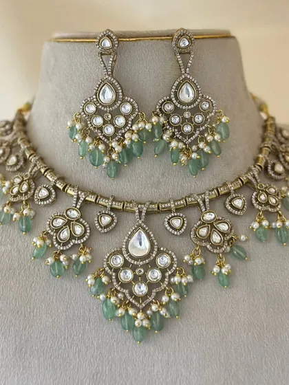 A lovely antique-finish necklace set with mint-green beads and pearl accents. The floral and heart-shaped motifs add a touch of romance.