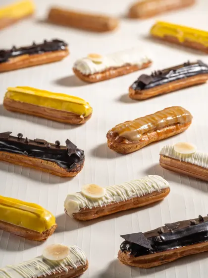 A pattern of assorted eclairs with different toppings like chocolate, white chocolate, and caramel, creating a visually interesting flat lay.