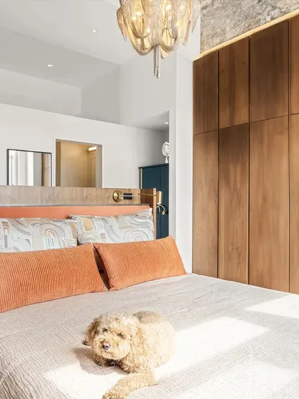 The master bedroom in the New York apartment features a custom multi-functional headboard we designed to save space. It includes a ledge for bedside items and incorporates a desk on its reverse side, all while framing the stunning city skyline view.