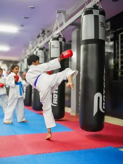 A young karate student in a blue belt executes a precise kick on a heavy bag. This image captures the focus and power that comes from consistent training and practice.