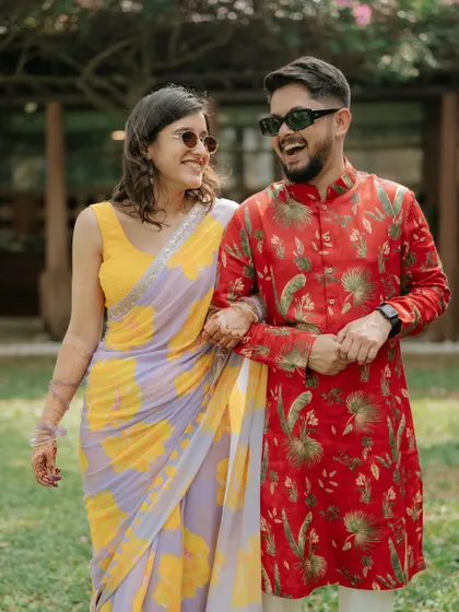 A fun, candid walking shot of a couple in colorful outfits, sharing a laugh. Their sunglasses add a cool, modern touch.