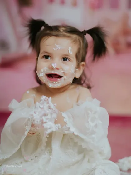 The smile says it all. This little girl, with her adorable pigtails and lacy white dress, is loving every second of her pink themed cake smash.
