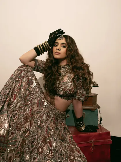 A full-look bridal portrait with a modern, edgy twist. The combination of a traditional lehenga with black gloves creates a unique and memorable fashion statement.