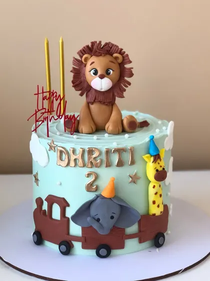A cute animal train cake, with a lion driving and an elephant and giraffe as passengers.