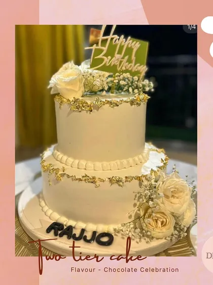 An elegant two-tier birthday cake in white, accented with gold leaf details and fresh white roses. The personalized name adds a special touch to this sophisticated design.
