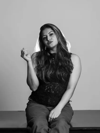 A seated black and white portrait in the studio. The monochrome conversion brings out the texture of the clothing and the subtle backlighting on the hair.