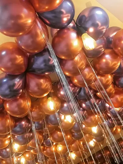 A close-up view of a ceiling decoration showing how I mix metallic balloons with warm Edison bulbs. This combination creates a beautiful, glowing effect for any evening party or celebration.