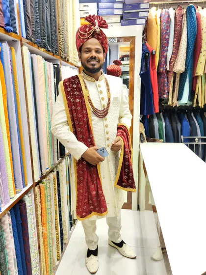A smiling groom trying on his final wedding attire in my studio. This classic off-white sherwani is perfectly complemented by a rich maroon velvet stole, creating a sophisticated contrast.