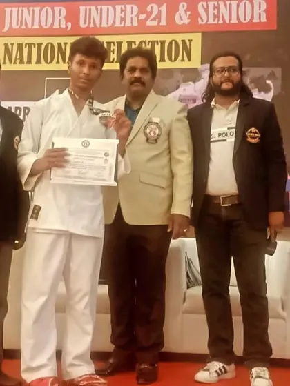 A student proudly displays his medal on stage with officials at the 15th State Level Karate Championship.