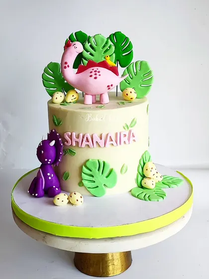 Who says dinosaurs can't be cute? This adorable dinosaur-themed cake was for Shanaira's birthday, featuring friendly pink and purple dinos among tropical leaves.