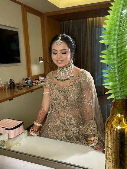 Riya admiring her final bridal look in the mirror. The soft lighting highlights her glowing skin and the intricate details of her makeup and hair.