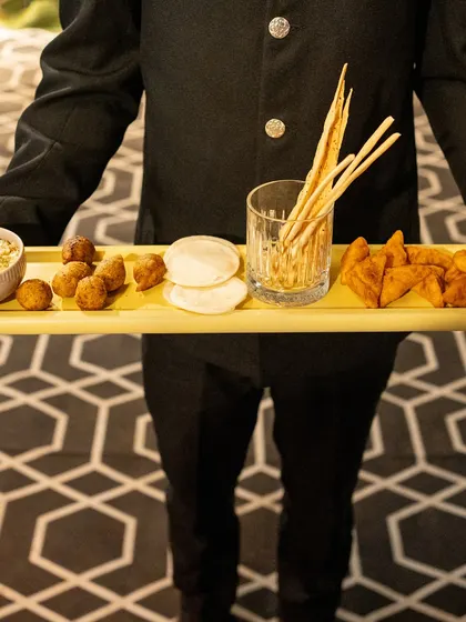 A server presents a tray of assorted appetizers, including arancini and samosas. This showcases our ability to blend international and Indian flavours seamlessly.