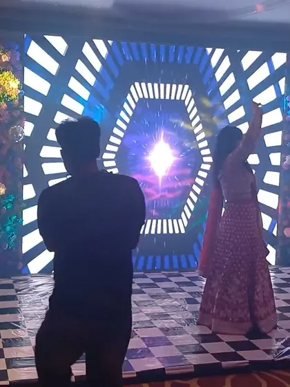 A high-energy Sangeet stage with a large LED screen displaying psychedelic patterns and a checkered dance floor.