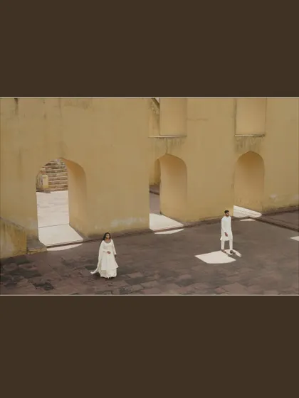 An architectural wide shot in Jaipur, where the couple stands apart yet connected by the space. This artistic composition uses shadows and light to create a dramatic effect.