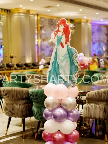 A themed table centerpiece featuring a cutout of Princess Ariel from The Little Mermaid, placed on a column of pink, purple, and silver balloons.