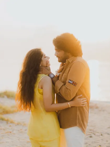 A beautiful golden hour portrait on the beach. The warm, setting sun creates a stunning backlight, highlighting the couple's connection and the romantic atmosphere.