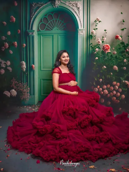A vision in red. This mother-to-be looks absolutely radiant in a voluminous red tulle gown, set against a classic green door and floral wall.