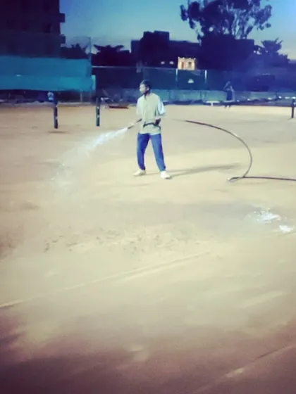 Evening maintenance in progress as a staff member waters the clay court to prepare it for the next day's play.