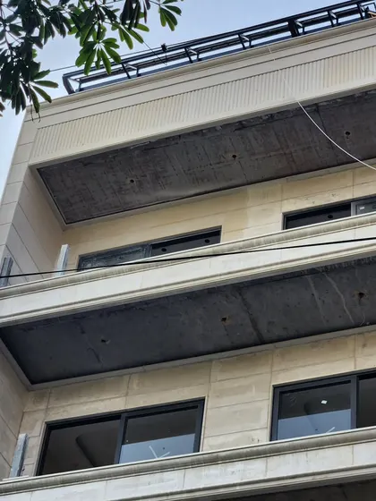 A residential building facade during the later stages of construction. The stone cladding is on, but the balconies' concrete ceilings are still exposed, showing the layers of the process.
