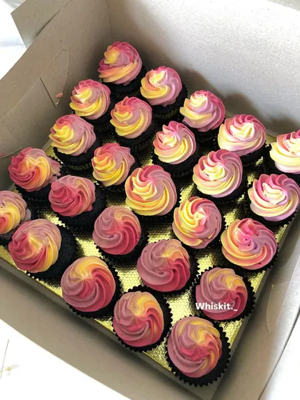 A large order of mini cupcakes with a vibrant, multi-colored swirl frosting. These are great for filling up a dessert table with a pop of color.