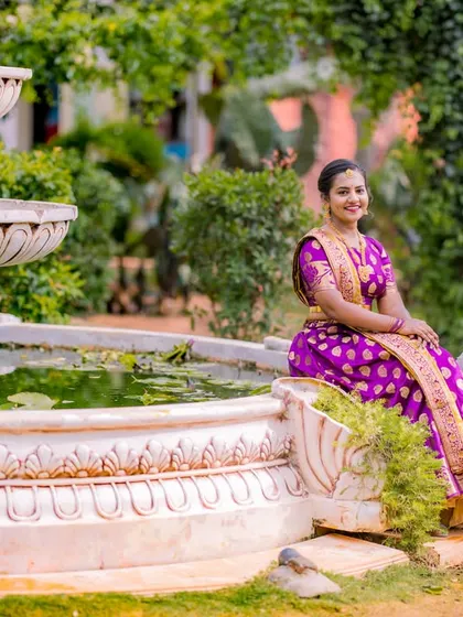 A serene portrait of a couple by a fountain. The bride's purple saree and the groom's golden kurta create a regal and elegant look.