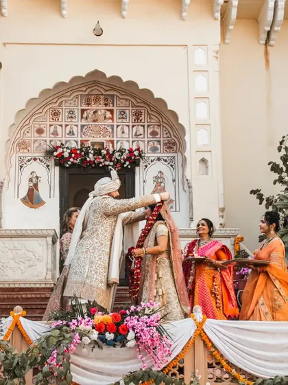 The groom places the garland on the bride during their daytime wedding ceremony at a heritage location.