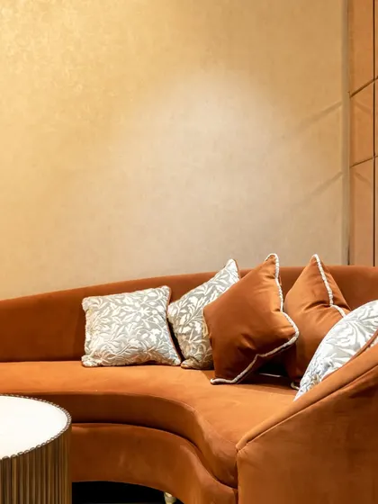 Comfort is key to a luxurious shopping experience. This custom-designed curved sofa in a rich terracotta velvet provides a soft, inviting seating area, set against a wall with subtle, textured wallpaper.