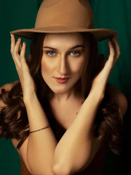 A classic portrait with a fedora hat, giving it a cool, bohemian vibe. The dark green background makes the warm tones of the outfit pop.