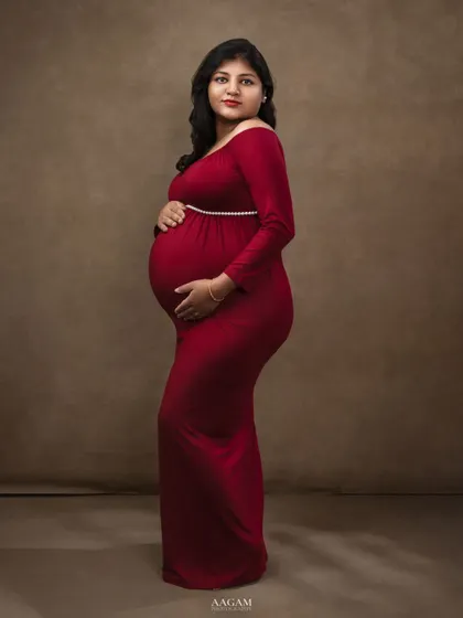 This side profile in a simple red gown against a solid backdrop emphasizes the beautiful silhouette of pregnancy.