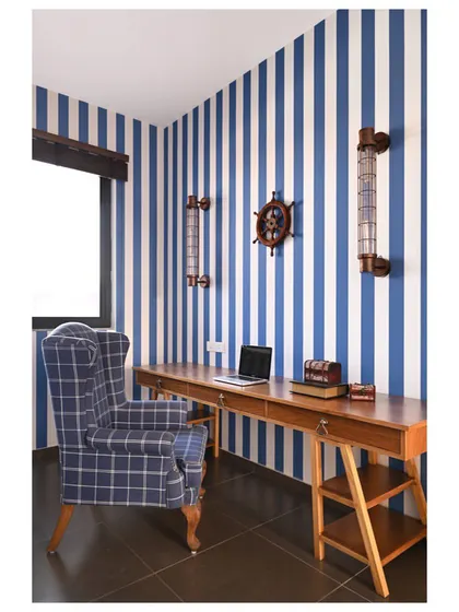 We designed this study to reflect the owner's personality as a Merchant Navy officer. The blue and white striped wallpaper, 9-foot custom desk, and vintage marine accessories create a strong, thematic workspace.