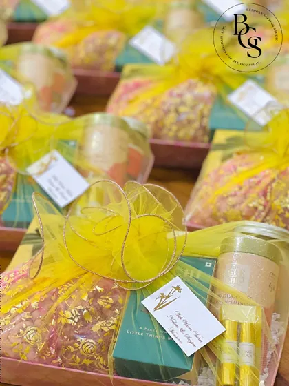 A festive hamper wrapped in bright yellow organza. The sheer fabric allows the contents to be partially visible, building anticipation, while the gold-edged ribbon adds a touch of celebratory sparkle.
