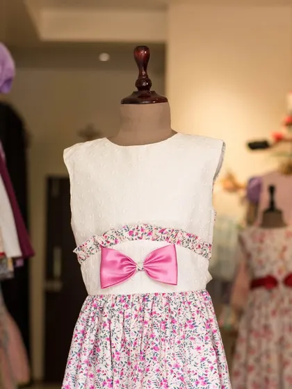 A charming dress featuring a white textured bodice and a pink floral skirt. The bright pink bow at the waist ties the two parts together beautifully.