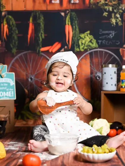 This little chef is busy mixing up something delicious. The rustic wooden backdrop and vegetable props make this kitchen theme feel so real and fun.