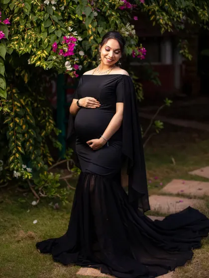 A gentle, smiling portrait of the mom-to-be in a garden setting, the black gown contrasting beautifully with the surrounding greenery.
