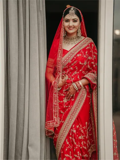 A classic bridal portrait, capturing the bride's radiant smile and the exquisite details of her red wedding saree.