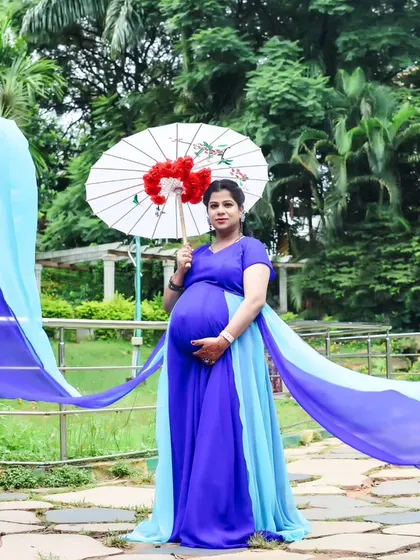 A solo portrait of an expectant mother in a blue trail gown, holding a traditional paper umbrella in a serene garden setting.