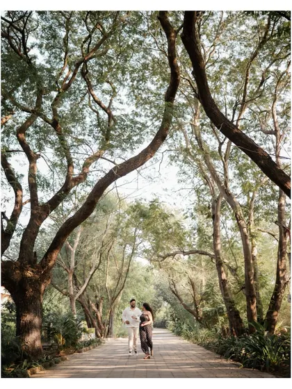 A wide shot of the couple walking together on a path surrounded by lush trees, perfect for a romantic pre-wedding album.