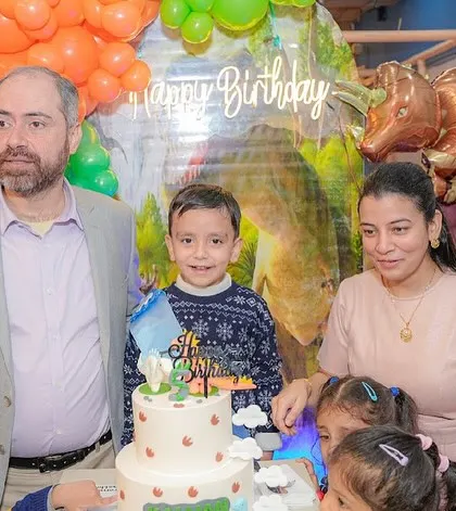A family poses behind the cake at a dinosaur-themed birthday party.