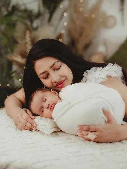 A mother and her newborn baby sharing a peaceful moment. The warm, soft lighting and boho decor create a cozy and intimate atmosphere.