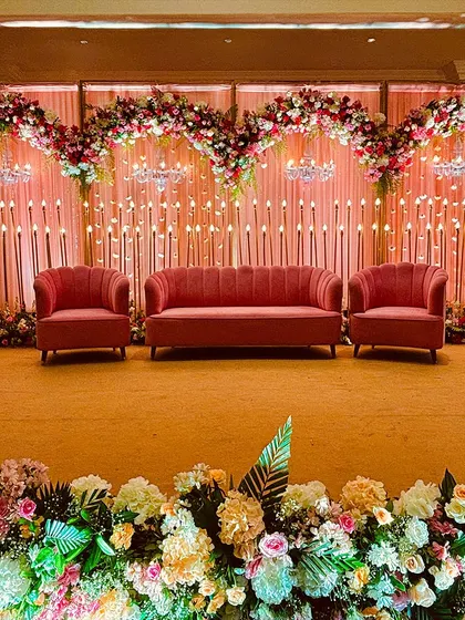 A romantic reception stage with three heart-shaped floral arches, mini chandeliers, and a wall of candle lights, all in a beautiful blush pink theme.