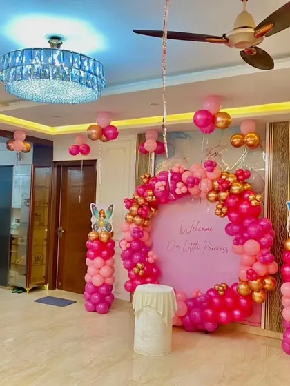 A "Welcome Our Little Princess" themed decoration for a home party. This setup features a beautiful pink and gold circular backdrop, fairy character cutouts, and balloon pillars, perfect for celebrating a new arrival or a birthday.