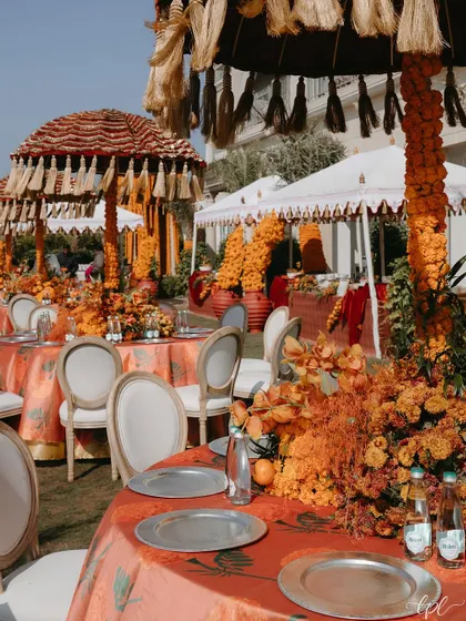 The outdoor setup for the marigold-themed Mehendi, with tassel-fringed umbrellas and custom-printed tablecloths creating a cohesive, festive look.