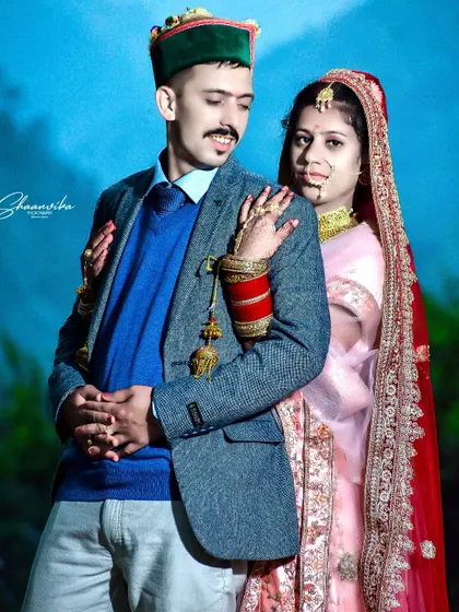 A lovely couple's portrait showcasing their traditional Himachali wedding outfits. The bright blue background makes their attire stand out beautifully.