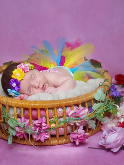 A one-month-old baby girl in a rainbow tutu, sleeping in a basket decorated with flowers.